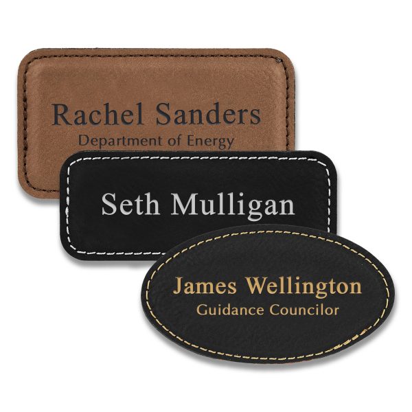 Rectangle and oval shaped black and brown leather name tags with engraved lines of text.